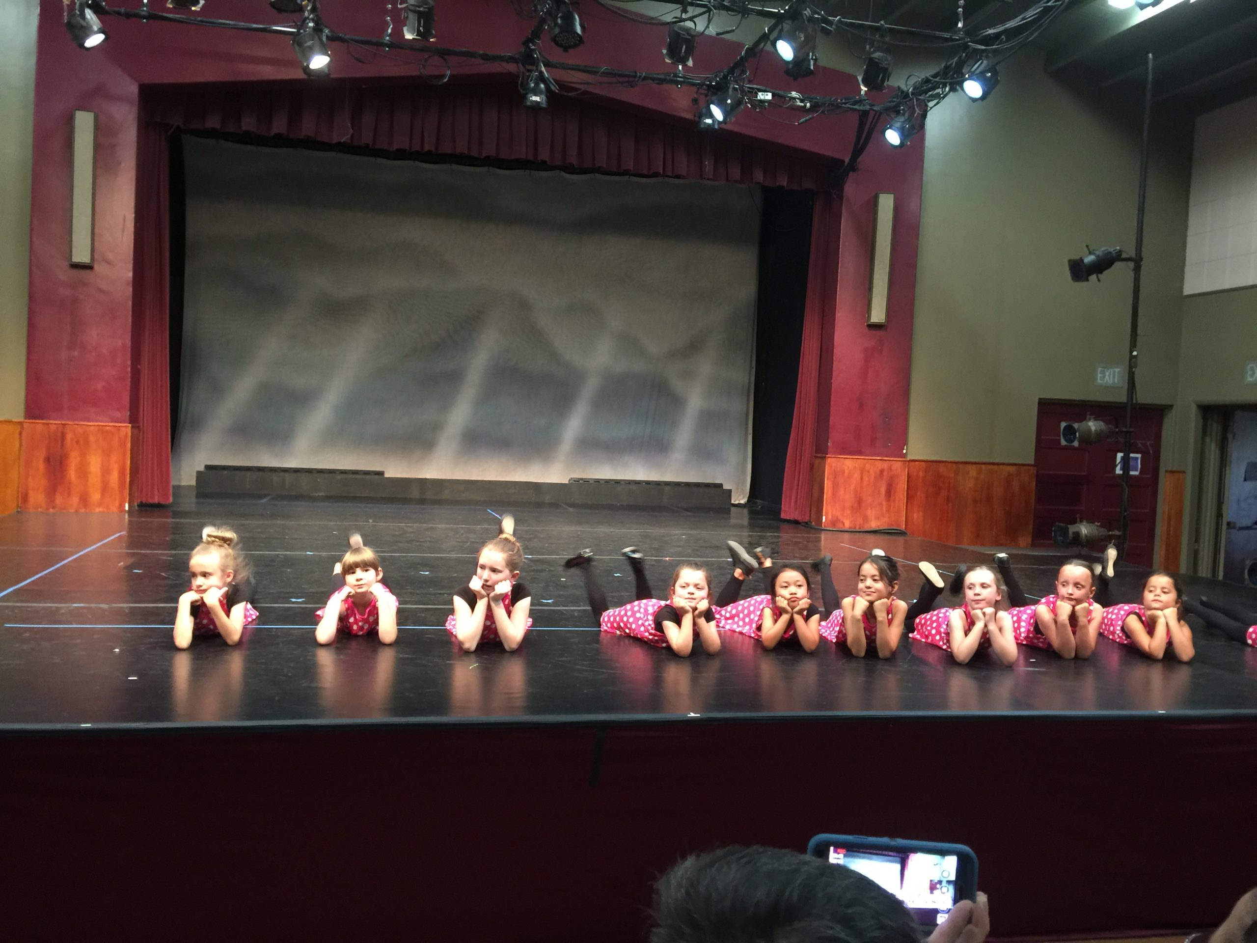 Young dancers laying chest down with feet raised in air on stage